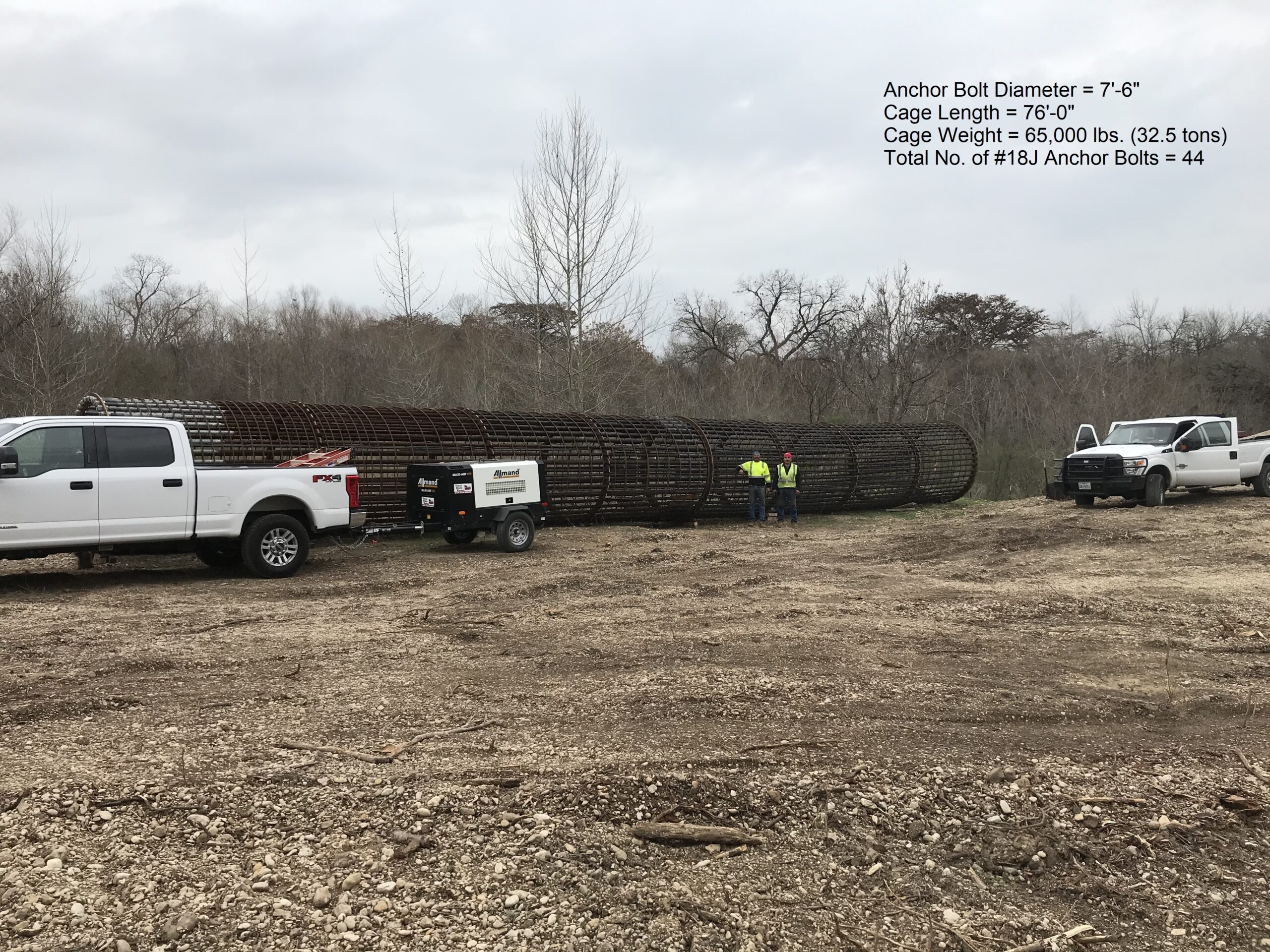 Heavy-duty anchor bolts are displayed on-site, while workers in safety vests oversee their setup next to pickup trucks and a trailer.